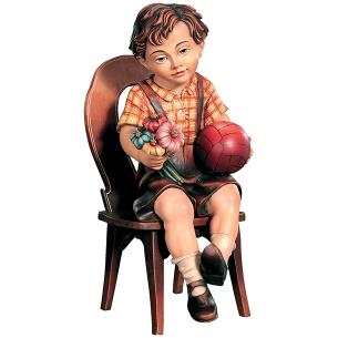 Bambino seduto con pallone e fiori su sedia